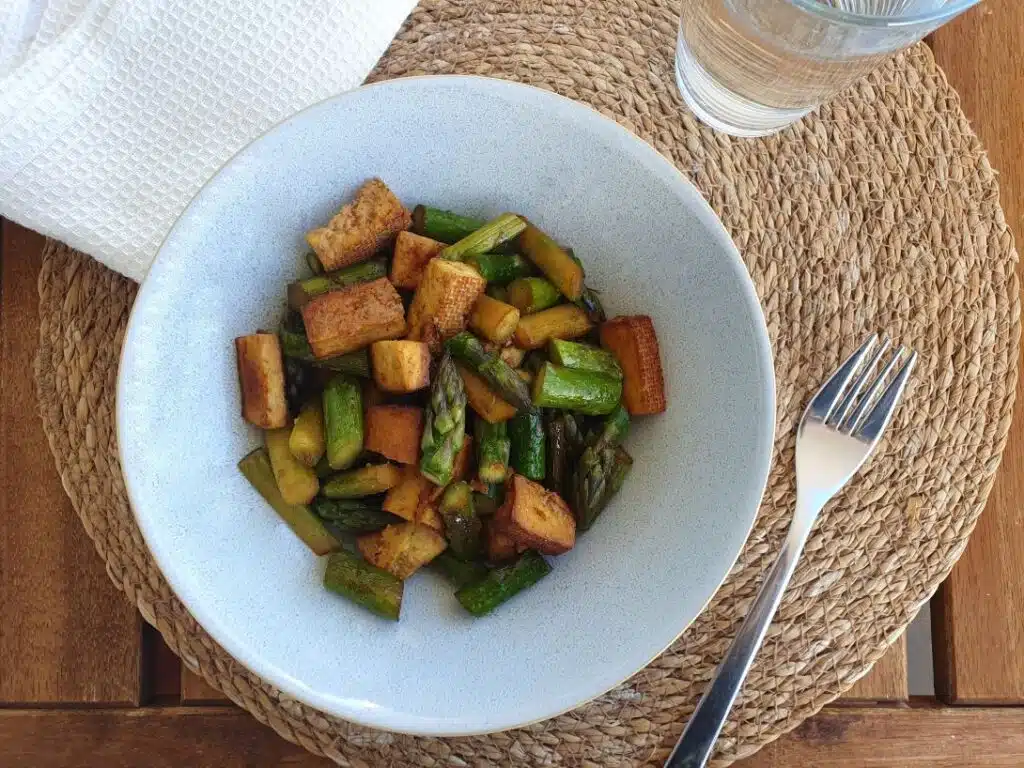 Grüner Spargel Pfanne mit Tofu in einem Teller auf einem braunen Tisch